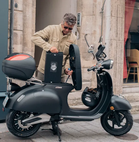 Homme en ville sortant de son scooter sa batterie amovible.